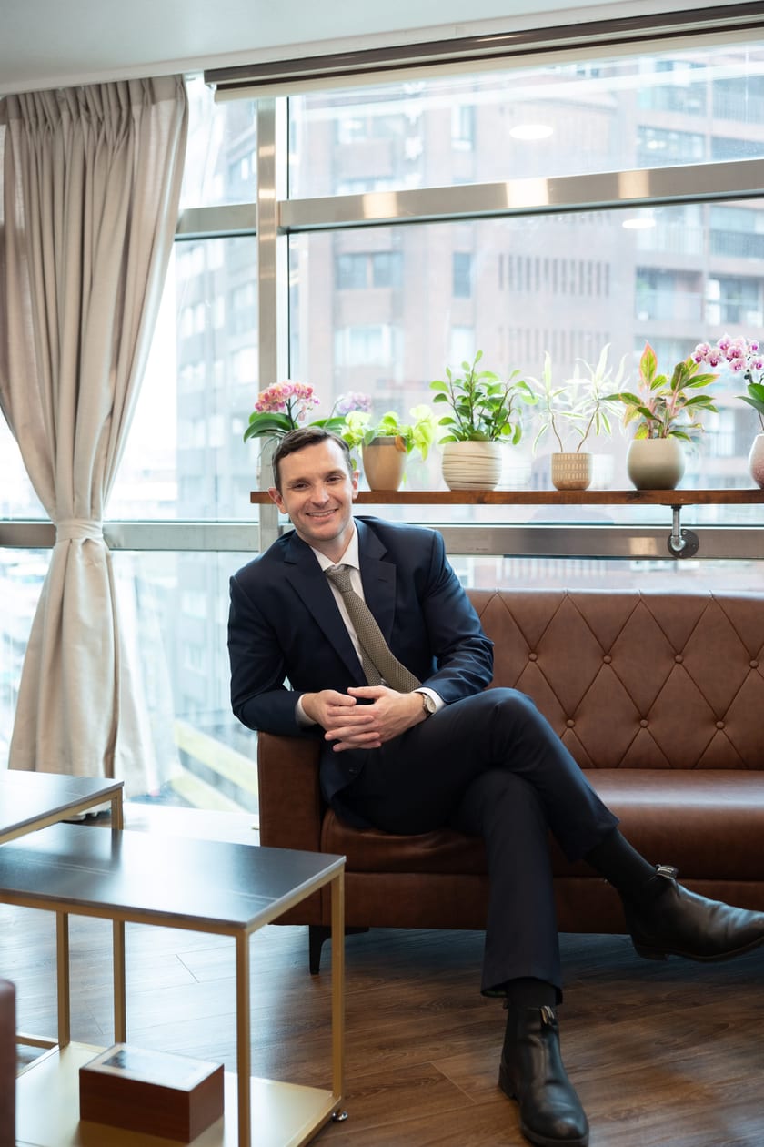 Mr. Harris, Founder of Harland Education, seated in the Harland office with orchids and city windows behind him.